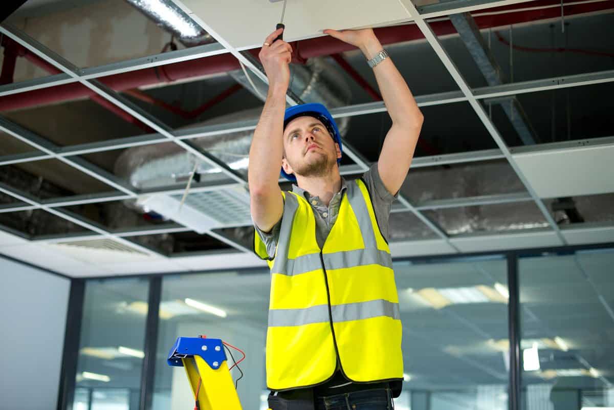 Electrician installing wiring above a commercial drop ceiling for building electrical infrastructure.