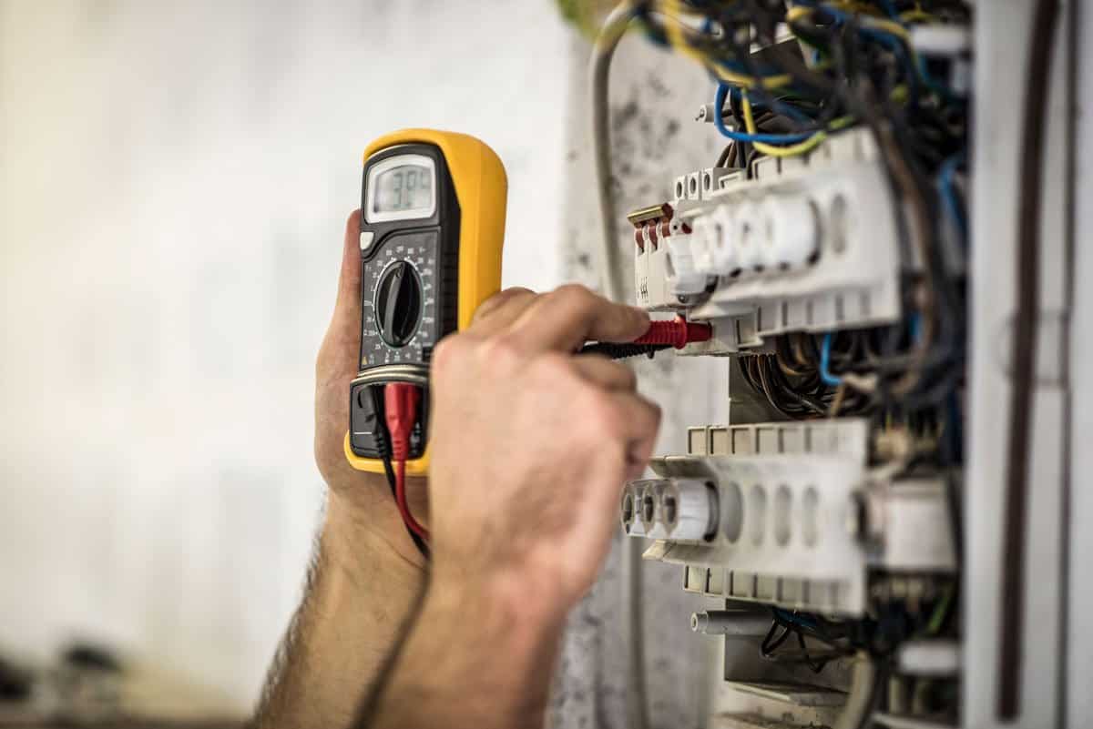 Technician testing voltage inside an electrical breaker panel using a digital multimeter.