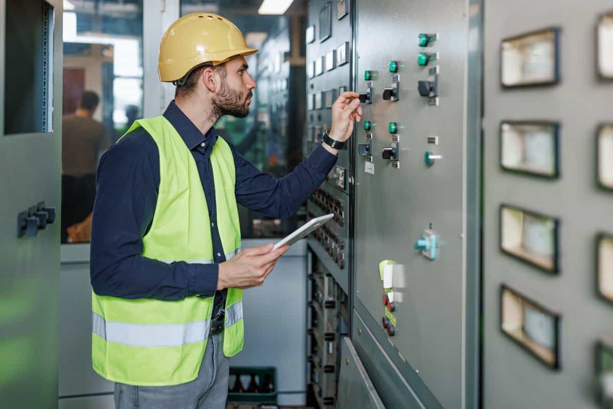 Industrial technician monitoring and adjusting electrical control systems in an automation panel.
